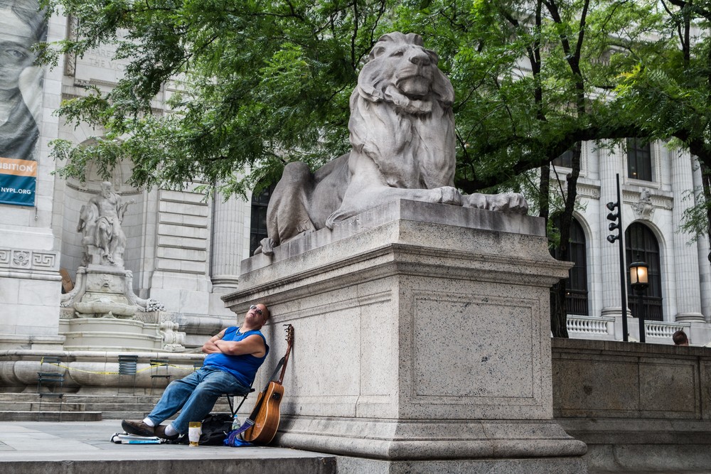 Lion and sleeping musician in front of the Library.<br />July 12, 2017 - Manhattan, New York City, New  York.