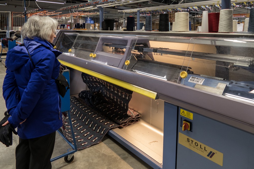 Joyce watching a knitting machine spit out hundreds of puffins.<br />Kidka Wool Factory Shop.<br />April 18, 2017 - Hvammstangi, Iceland.